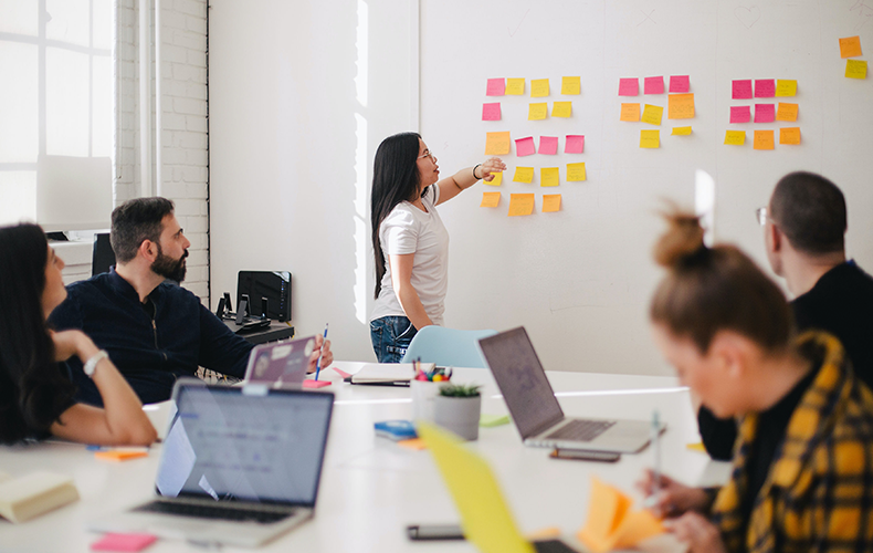 Photo of colleagues in meeting, reviewing post-it notes on wall