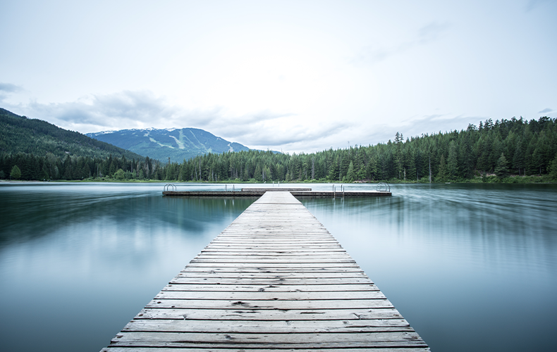 Image of a dock on a lake with trees and mountains in the distance