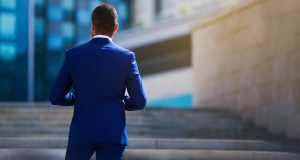 Man in blue suit facing office building stairs